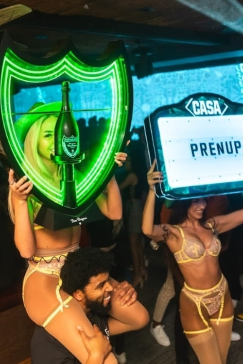 Performers in lingerie holding up illuminated signs and a Dom Pérignon shield at a lively nightclub celebration.