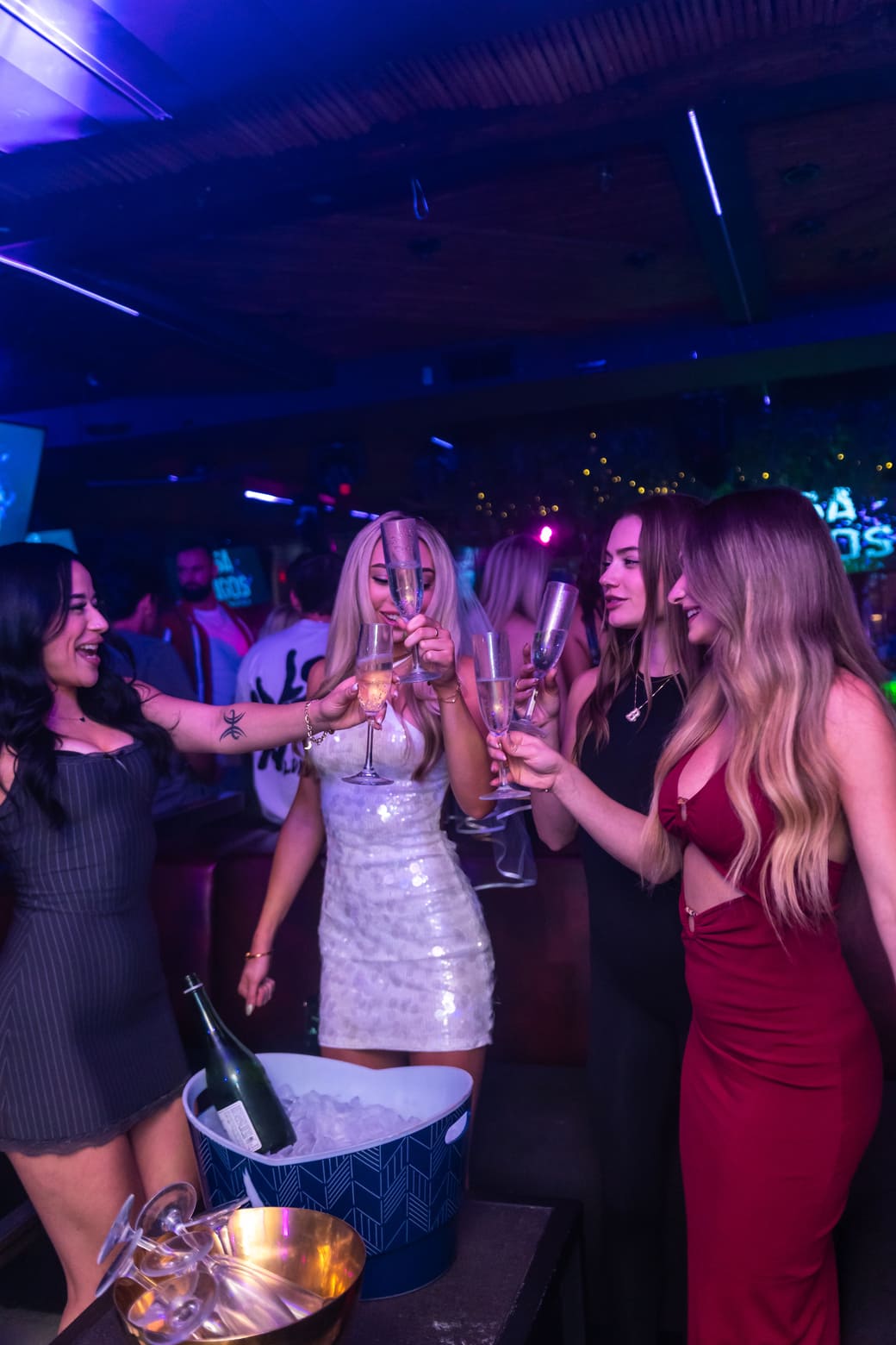 Group of women toasting with champagne glasses in a vibrant nightclub setting.