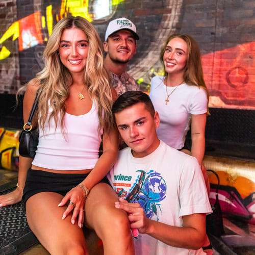 Two women and two men posing together with vibrant graffiti wall in the background.